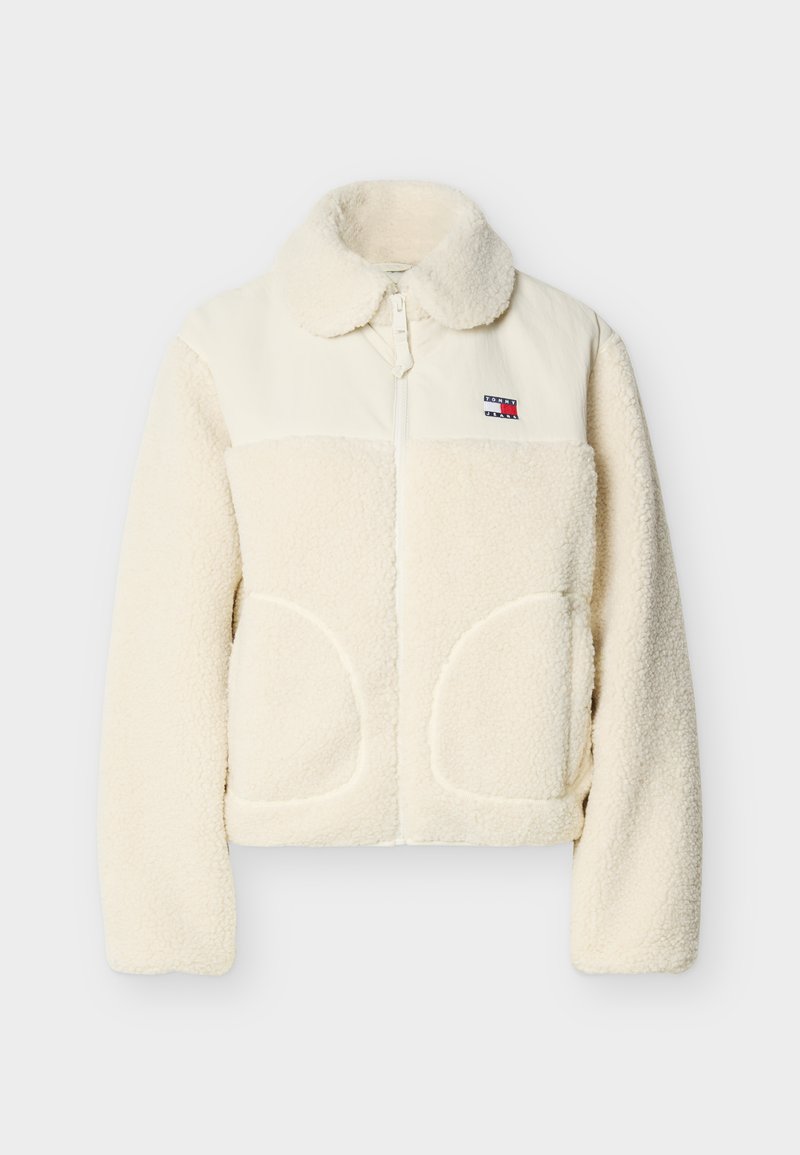 Sherpa-Jacke in Cremefarbe mit Stehkragen, Reißverschluss, großen Fronttaschen und einem kontrastierenden oberen Bereich aus glattem Stoff.