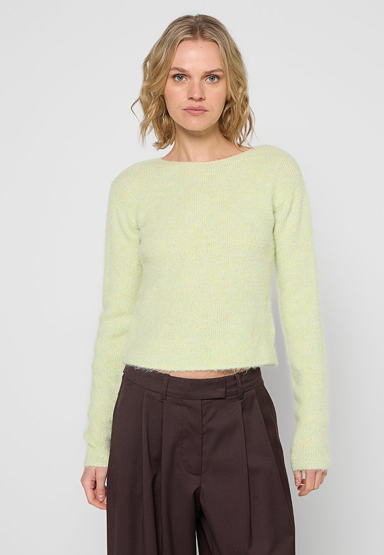 Hellgrüner, kurz geschnittener Pullover mit weicher, flauschiger Textur, langen Ärmeln und rundem Ausschnitt, kombiniert mit dunkelbraunen Hosen.