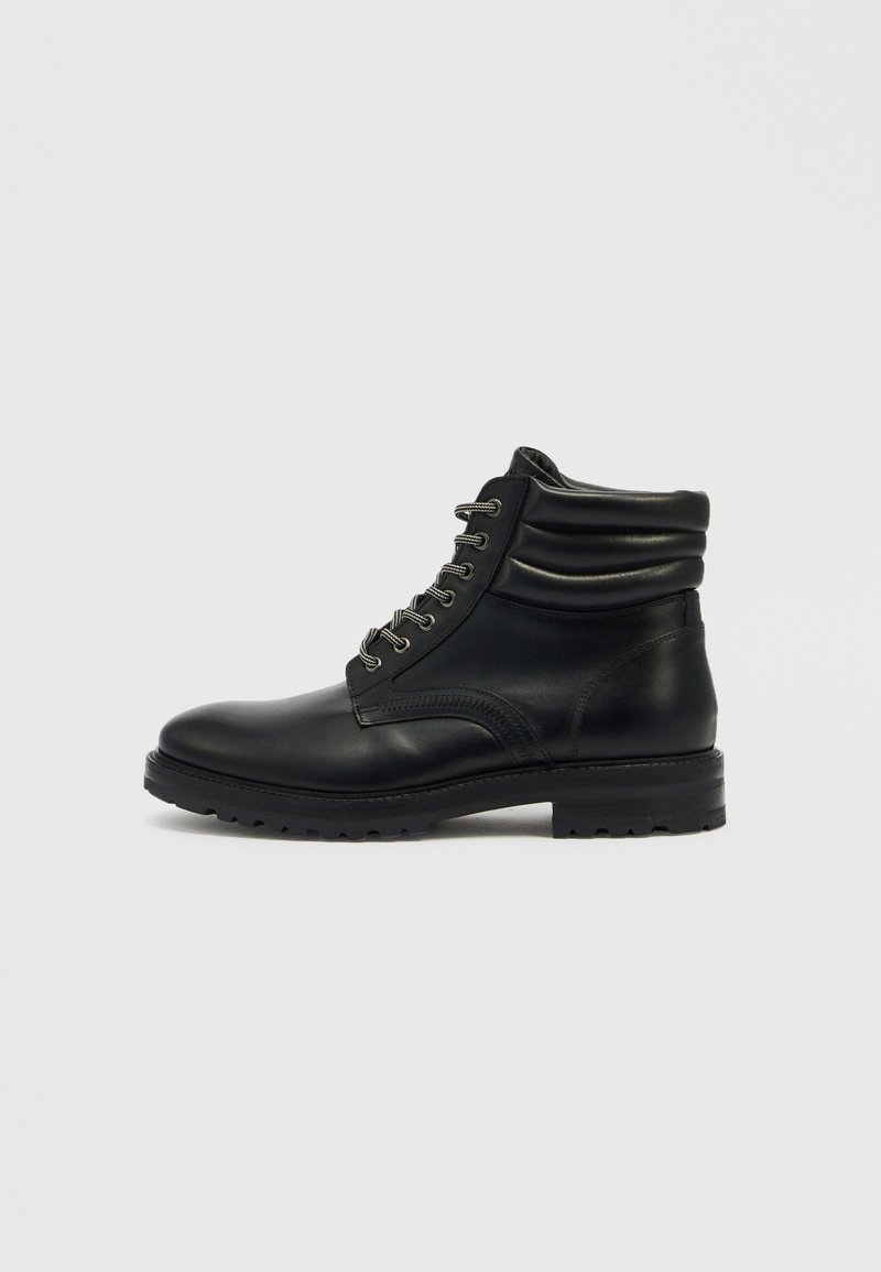 Schwarze Leder-Stiefeletten mit runder Spitze, Schnürdesign, lockerem Schaft und strukturierter Sohle. Mit silberner Hardware und Nahtdetails.
