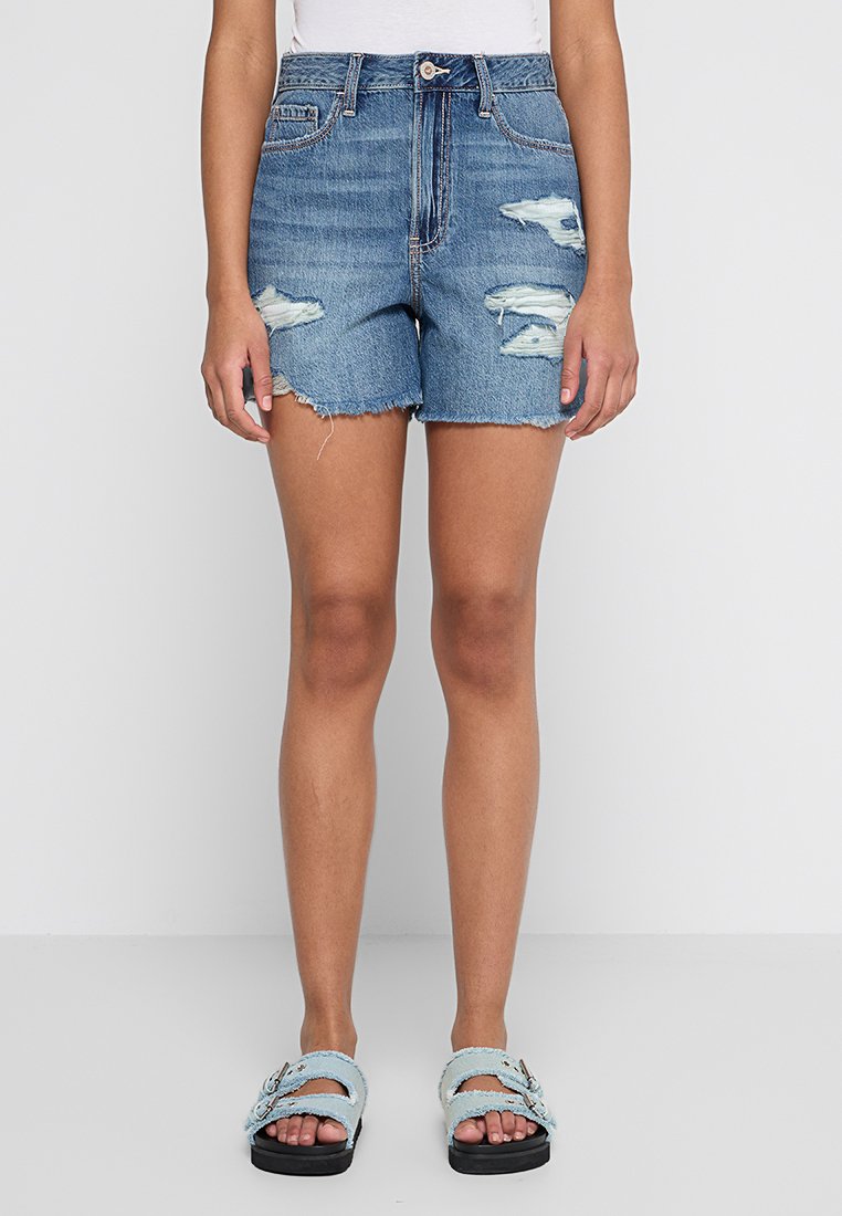 Helle Blaue Jeansshorts mit abgenutzten Details und ausgefranstem Saum. Kombiniert mit hellblauen Sandalen mit Schnallen und strukturierten Riemen.