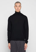 Schwarzer Rollkragenpullover mit gerippter Textur und langen Ärmeln. Enganliegendes Design mit flacher Strickkante. Getragen mit grauen Hosen.