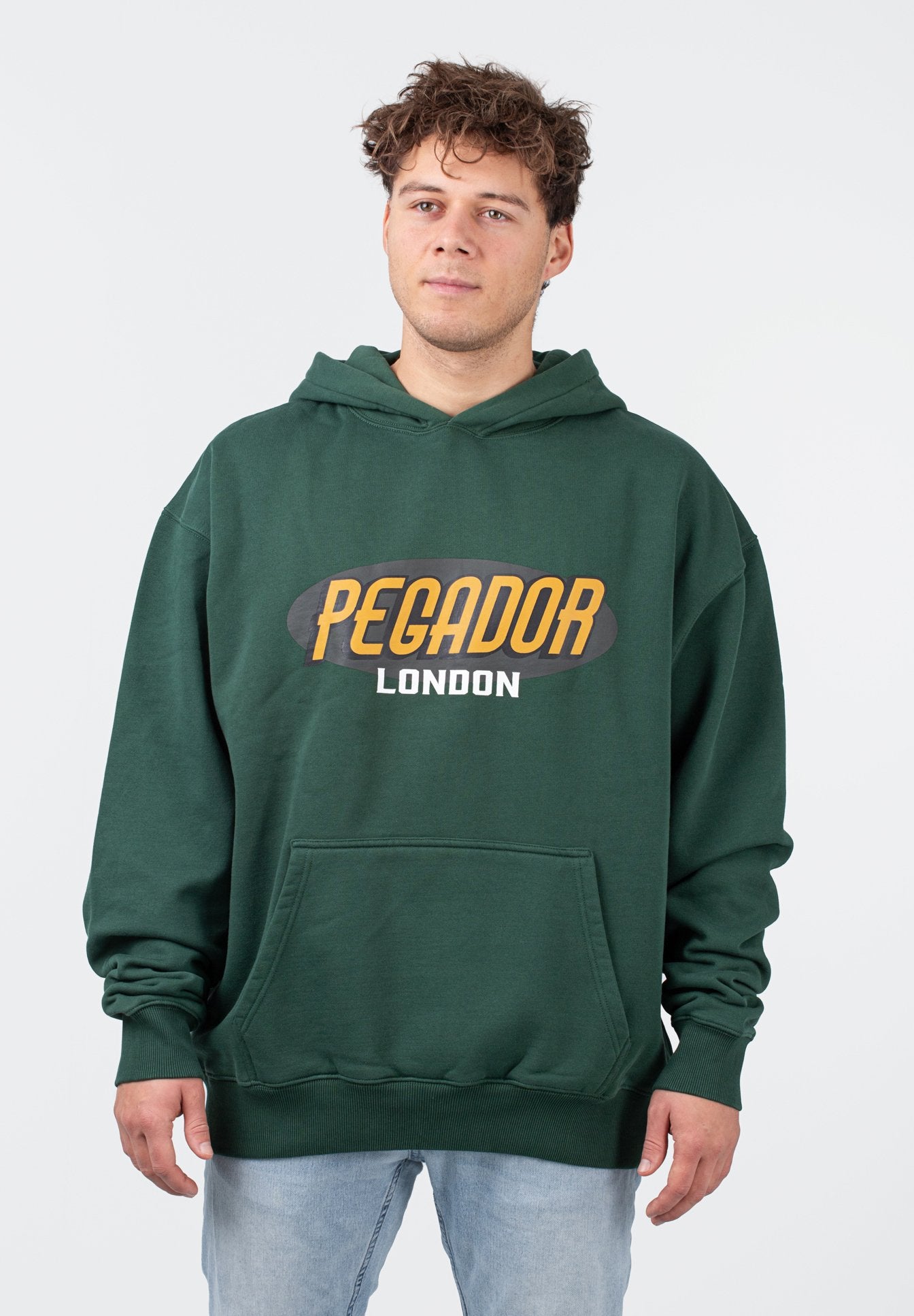 Grüner Kapuzenpullover aus Baumwollmischung mit großem "PEGADOR LONDON" Schriftzug in Orange und Weiß. Verfügt über eine Vordertasche und gerippte Bündchen.