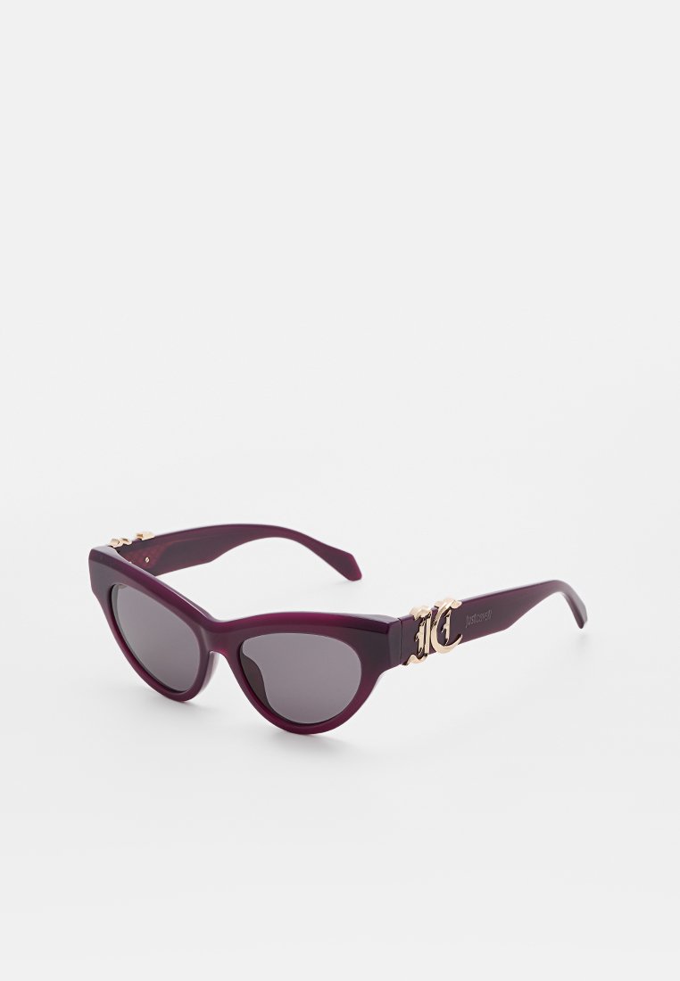 Dunkellila Cat-Eye-Sonnenbrille mit goldfarbenen, dekorativen Scharnieren und dunkel getönten Gläsern auf weißem Hintergrund.