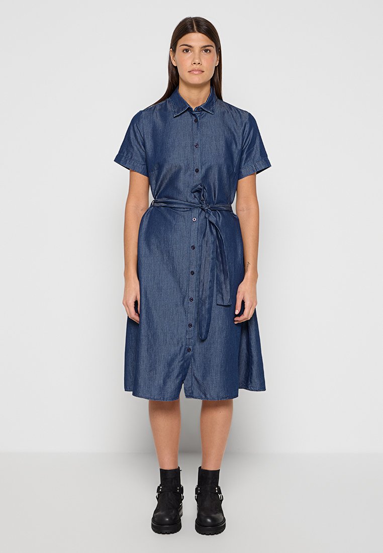 Jeanshemdkleid in Dunkelblau, kurze Ärmel, durchgehend geknöpft, Taillengürtel, knielang, glatte Textur, kombiniert mit schwarzen Stiefeletten.