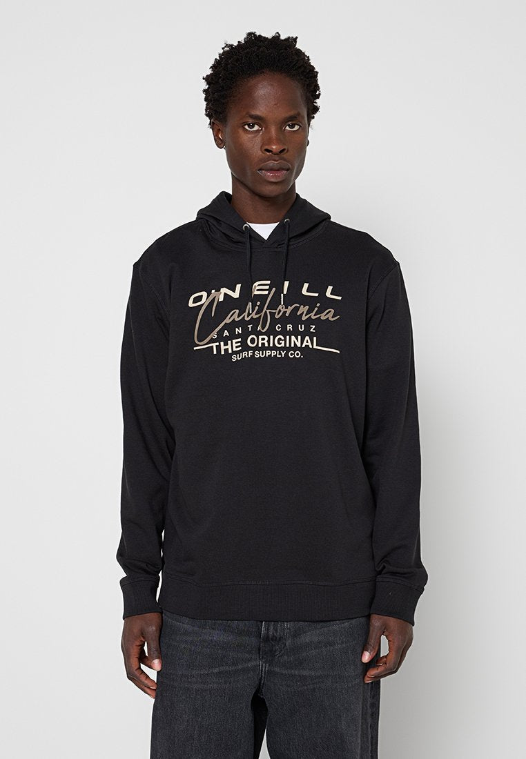 Junger Mann, der einen schwarzen O'Neill California Santa Cruz Hoodie und dunkle Jeans trägt, vor einem schlichten hellen Hintergrund steht.