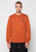 Rost-orange Langarm-Sweatshirt aus strukturiertem Stoff. Verfügt über einen Rundhalsausschnitt und ein marineblaues Logo auf der linken Brust. Mit gerippten Ärmelbündchen und Saum.