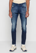 Dunkelblaue Jeans im Slim-Fit-Schnitt mit leichten Abnutzungen an den Oberschenkeln, fünf Taschen und einem Knopfverschluss. Getragen mit hellen Sneakers.