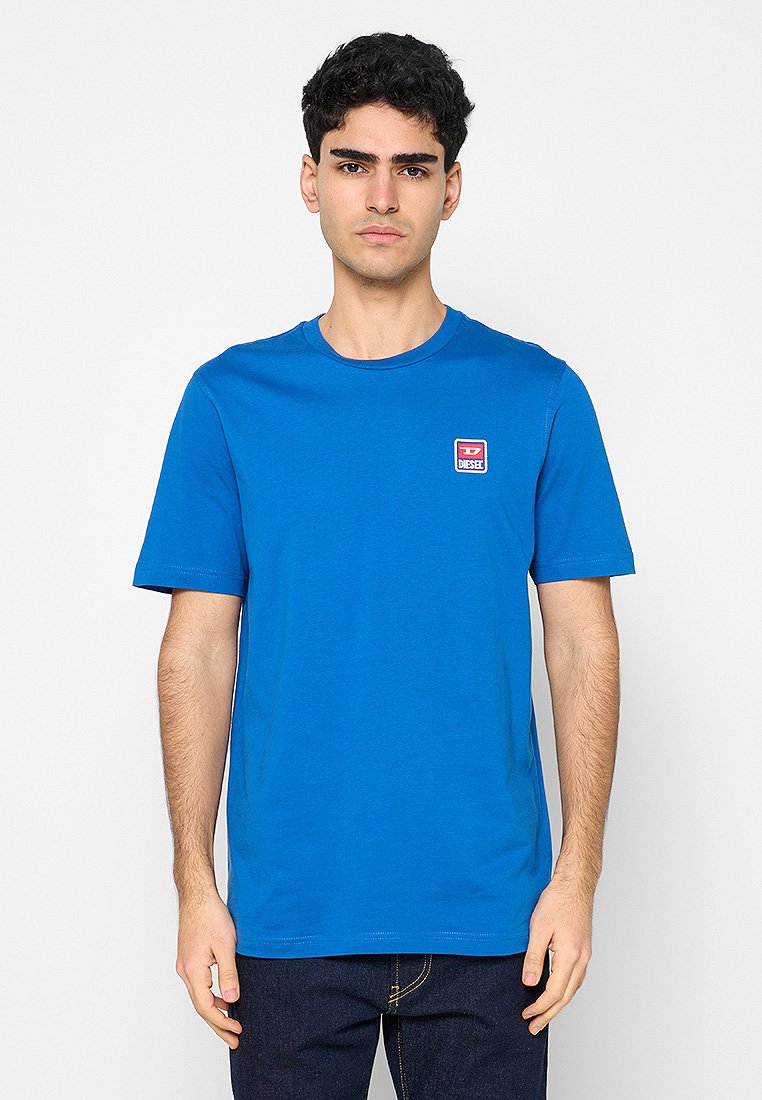 Blaues Baumwoll-T-Shirt mit Rundhalsausschnitt, kurzen Ärmeln und einem kleinen rot-weißen Logopatch auf der linken Brust. Glatte Textur, legere Passform.