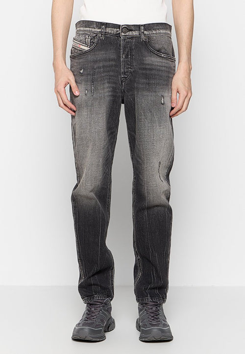 Schwarze Denim-Jeans mit einem distressed Finish, verblasster Textur, zwei vorderen Taschen und einem Knopfverschluss. Kombiniert mit grauen Sportschuhen.