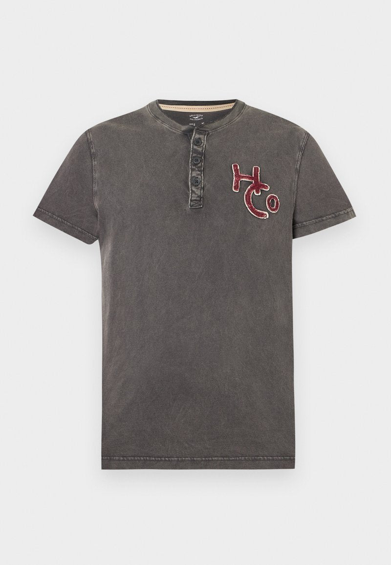 Dunkelgraues Henley-Shirt mit kurzen Ärmeln, drei Knöpfen und roter "HCo"-Stickerei auf der linken Brust.