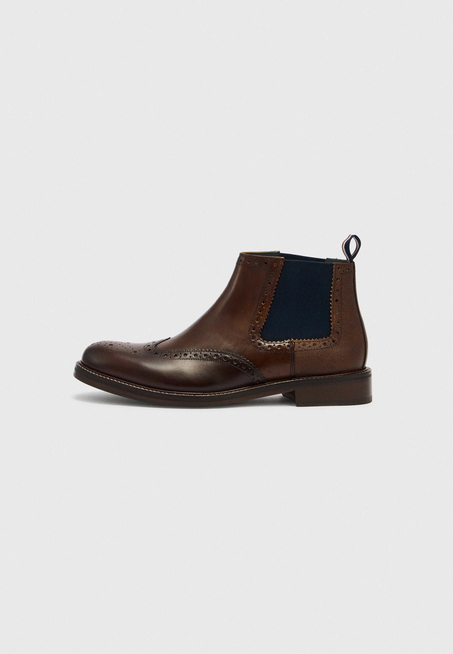 Brauner Chelsea-Stiefel aus Leder mit navyblauen elastischen Seitenteilen, perforierten Details und einer Lasche an der Ferse. Abgerundete Spitze und niedriger Absatz.