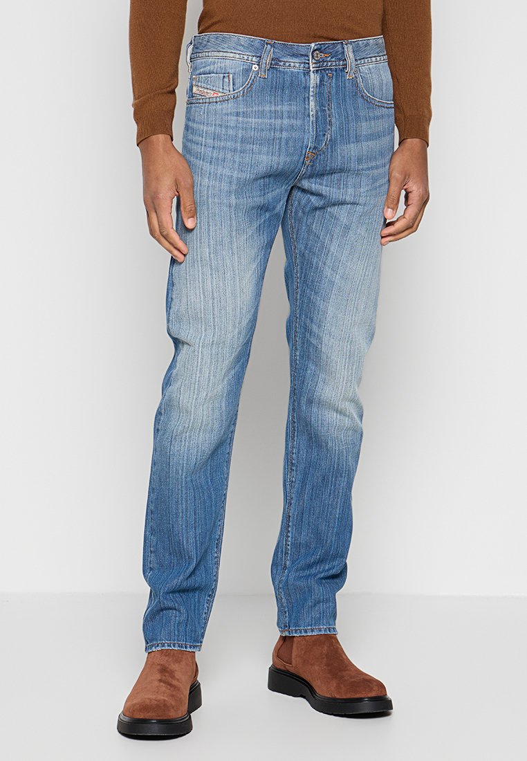 Verblasste blaue Jeans aus Denim mit geradem Schnitt, ausgestattet mit einem Fünf-Taschen-Design und dezenten Gebrauchsspuren, getragen mit braunen Wildleder-Stiefeletten.