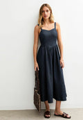 Dunkelblaues Denim-Maxikleid, Spaghettiträger, taillierter Oberteil, geraffte Taille, fließender Rock. Kombiniert mit braunen Sandalen und einer geflochtenen Tasche.