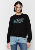 Schwarzes Sweatshirt mit einem Blumenmuster in Blau und Grün auf der Brust, Rundhalsausschnitt und gerippten Bündchen. Kombiniert mit hellen Denim-Hosen.