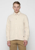 Beige Baumwolljacke mit Kragen, Frontknopfverschluss, zwei aufgesetzten Taschen und einem kleinen Logo-Detail an der unteren Seite.