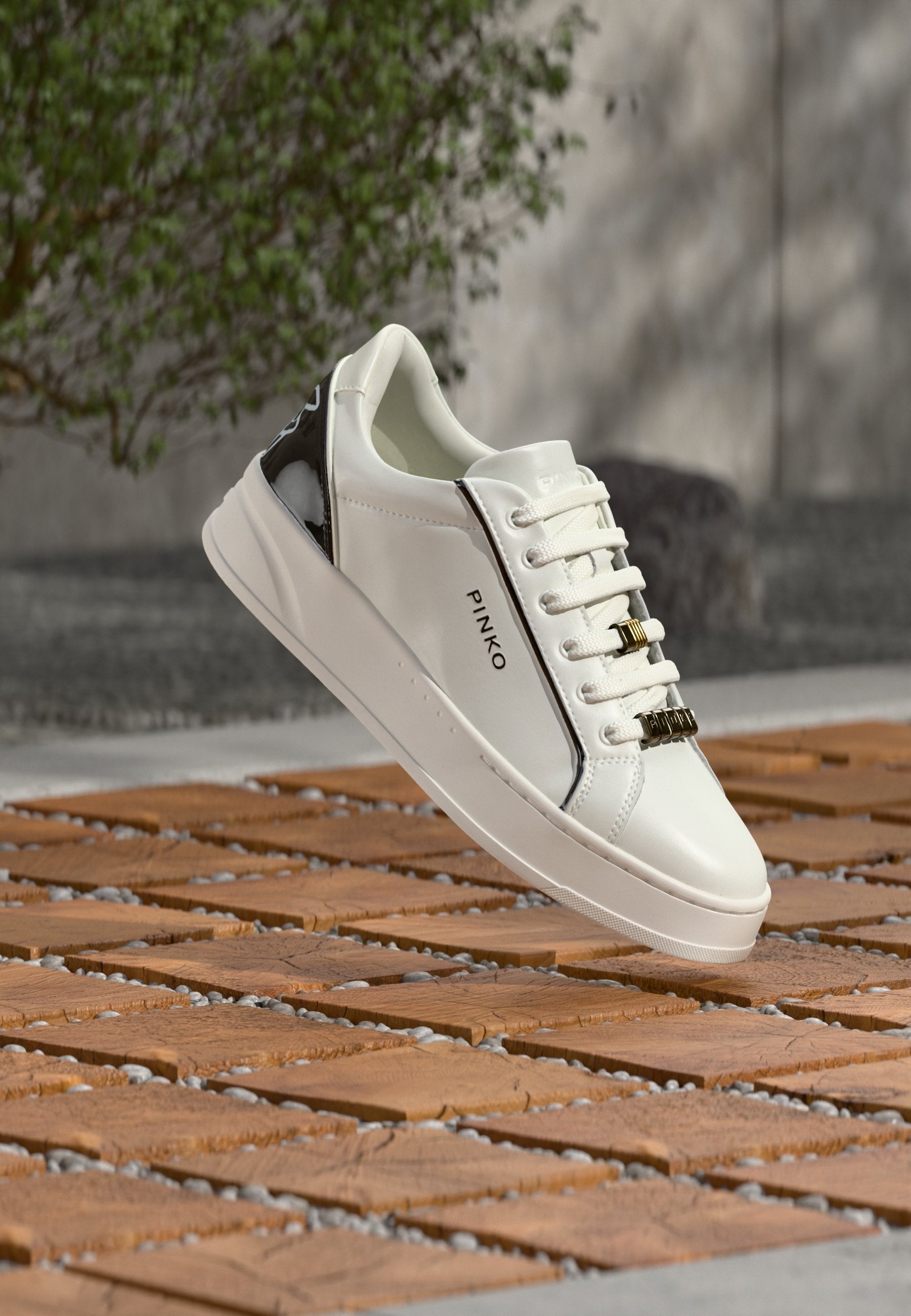 Weißer Ledersneaker mit schwarzen Lackakzenten, Schnürdesign, goldfarbenen Details, abgerundeter Spitze und profilierter Sohle. Markenname "PINKO" sichtbar.