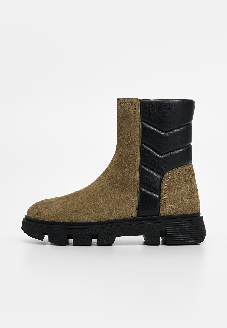 Wildleder-Stiefeletten in olivgrün mit einem schwarzen strukturierten Lederpanel hinten, ausgestattet mit einer gerippten Sohle und einer runden Zehenform.