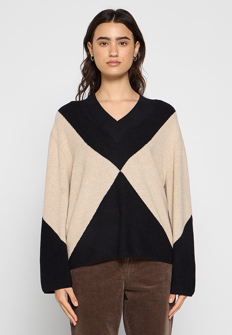 Beige und schwarzer V-Ausschnitt, oversized Pullover mit diagonaler Farbblockierung und geripptem Muster am Kragen und den Ärmeln.
