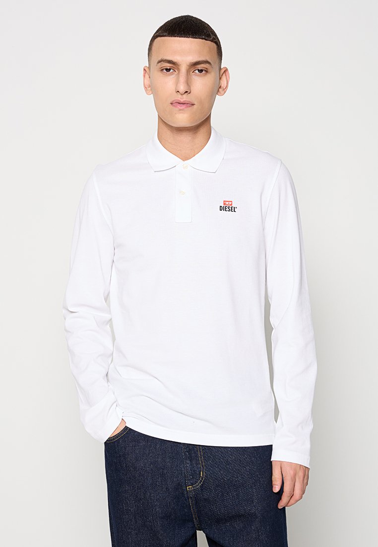 Weißes Langarm-Polo-Shirt mit drei Knöpfen und kleinem schwarzem Diesel-Logo auf der Brust, kombiniert mit dunkelblauen Jeans.
