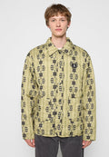 Junger Mann in einer hellgrünen, gesteppten Jacke mit schwarzen geometrischen und floralen Mustern, Fronttaschen und Druckknöpfen.