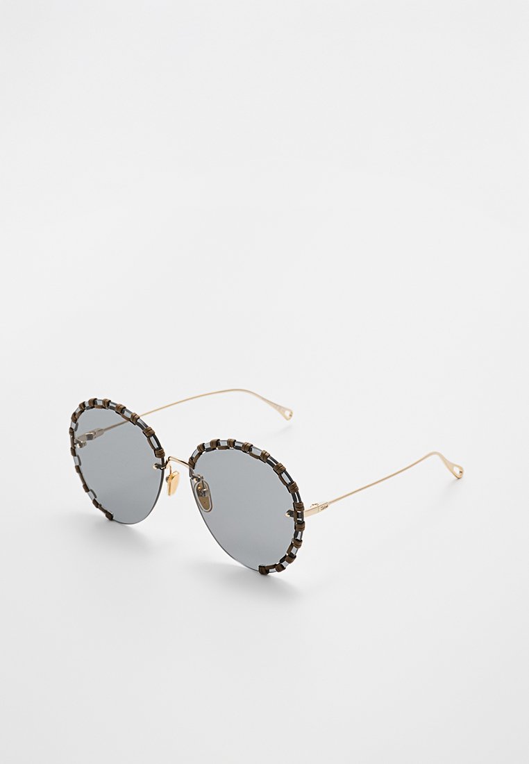 Runde Sonnenbrillen mit grauen Gläsern, goldenem Metallrahmen und einer strukturierten schwarzen Perlenakzent entlang des Rahmens. Leichtes Design mit dünnen Bügeln.