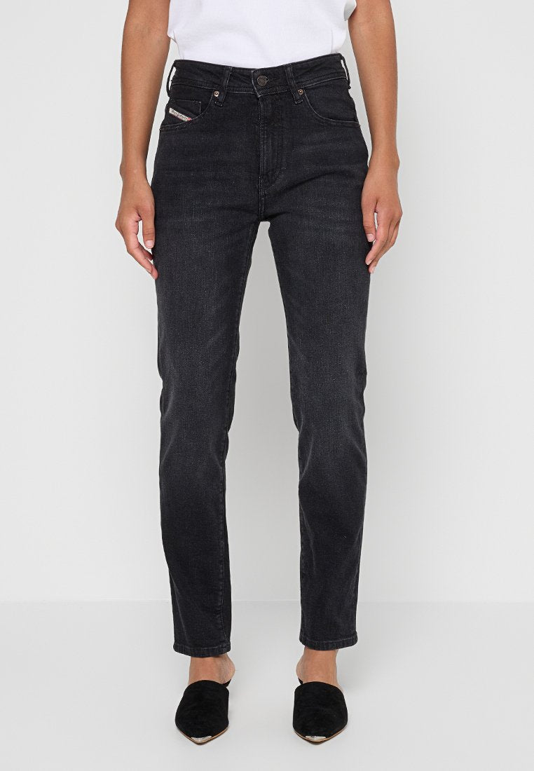 Schwarze Denim-Jeans mit schmaler Passform, mittelhohem Bund, fünf Taschen und dezenten Stickdetails. Getragen mit schwarzen Schuhen.
