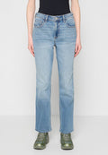 Hellblaue Jeans mit geradem Bein, getragen mit grünen Turnschuhen und einem schwarzen Oberteil, von der Taille bis zu den Füßen vor einem einfarbigen Hintergrund gezeigt.
