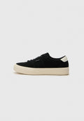 Schwarze Wildleder-Sneaker mit einer dicken beigen Gummisohle, runder Zehenpartie und schwarzen Schnürsenkeln. Auf der Ferse befindet sich ein weißer Akzent. Einfaches, klassisches Design.