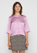Helles rosa Satin-Top mit kurzen Ärmeln, Rundhalsausschnitt und lockerer Passform, kombiniert mit einem schwarz-beige karierten Rock.