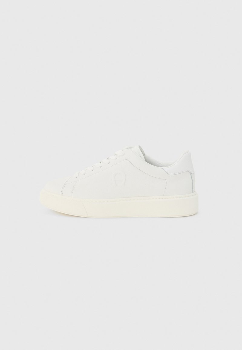 Weißer Ledersneaker mit niedrigem Schaft, Schnürverschluss, gepolstertem Kragen und dicker elfenbeinfarbener Gummisohle, von der Außenseite auf grauem Hintergrund gezeigt.