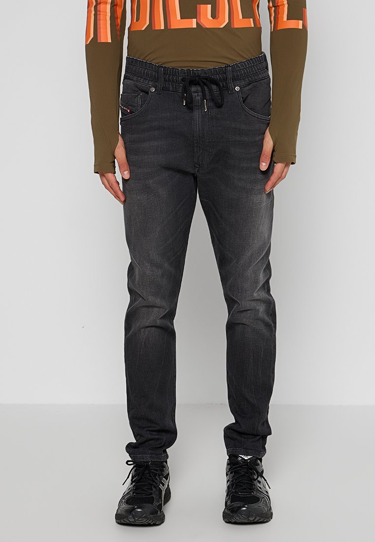 Dünne schwarze Denim-Jeans mit elastischem Bund und Kordelzug. Sie verfügen über fünf Taschen und eine verblasste Textur, kombiniert mit schwarzen Sneakern.