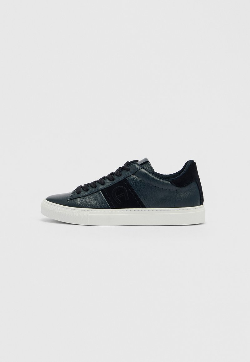 Niedriger schwarzer Ledersneaker mit schwarzen Wildledereinsätzen, schwarzen Schnürsenkeln und weißer Gummisohle, seitlich auf einfarbigem Hintergrund dargestellt.