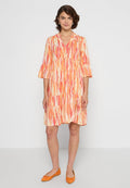 Kurzärmliges, orange- und pinkgestreiftes Kleid mit V-Ausschnitt, gestuftem Design und fließender Silhouette, kombiniert mit orangefarbenen Ballerinas.