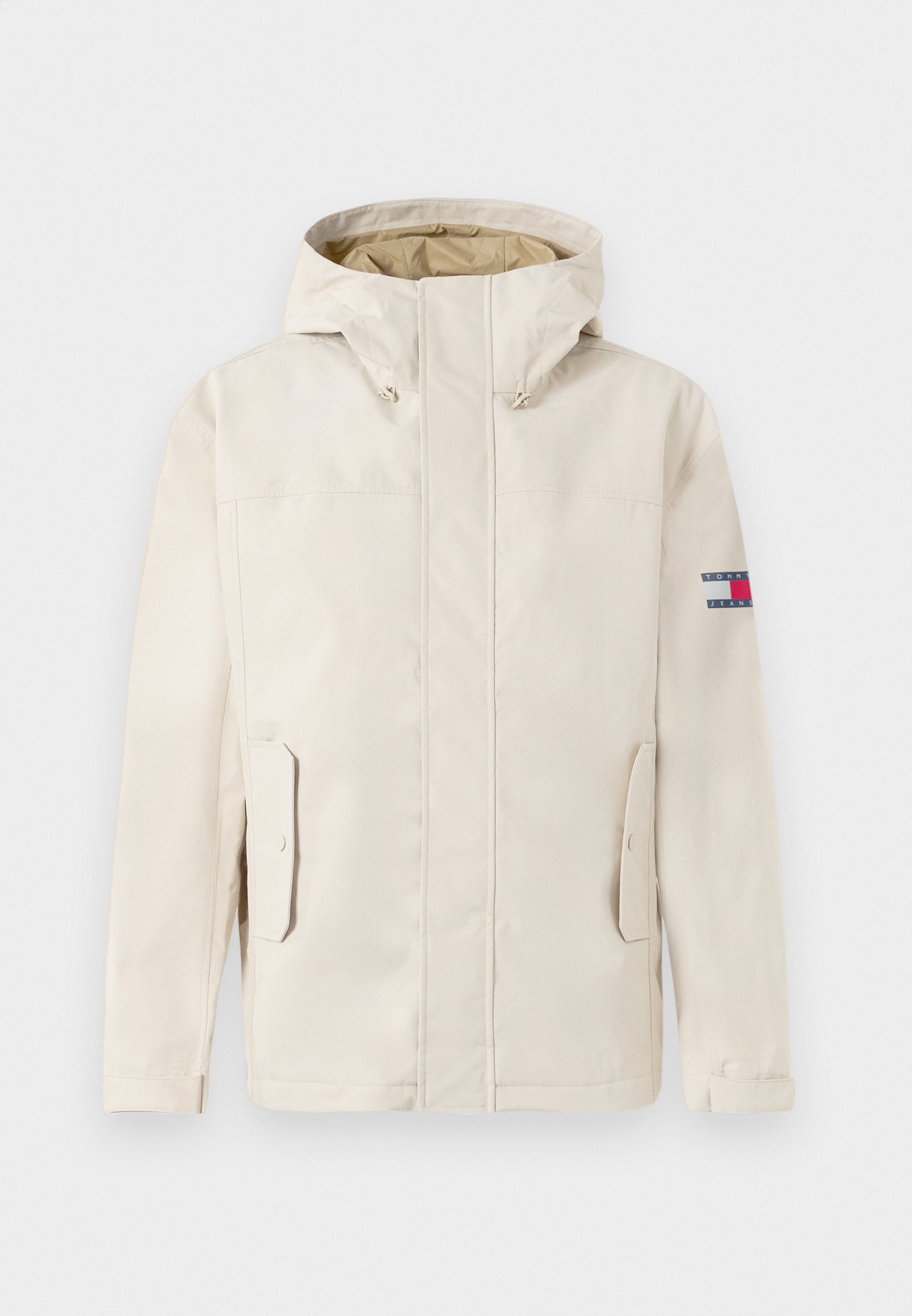 Beige Kapuzenjacke mit Fronttaschen und Klappenverschlüssen, langen Ärmeln und einem kleinen rechteckigen Logo-Patch am oberen linken Ärmel.