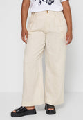 Beige Hochbundweite-Hosen mit weitem Bein und vorderen Falten, kombiniert mit schwarzen Plateausandalen und einem weißen T-Shirt mit Grafikdruck.
