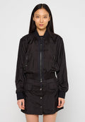 Schwarze Bomberjacke aus krinkligem Material, mit einem Reißverschluss vorne, zwei Reißverschlusstaschen und gerippten Bündchen. Kombiniert mit einem passenden Rock.