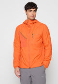 Mann trägt hellorange Hoodie mit Reißverschluss und Brusttaschen, kombiniert mit grauer Hose, steht vor hellem einfarbigem Hintergrund.