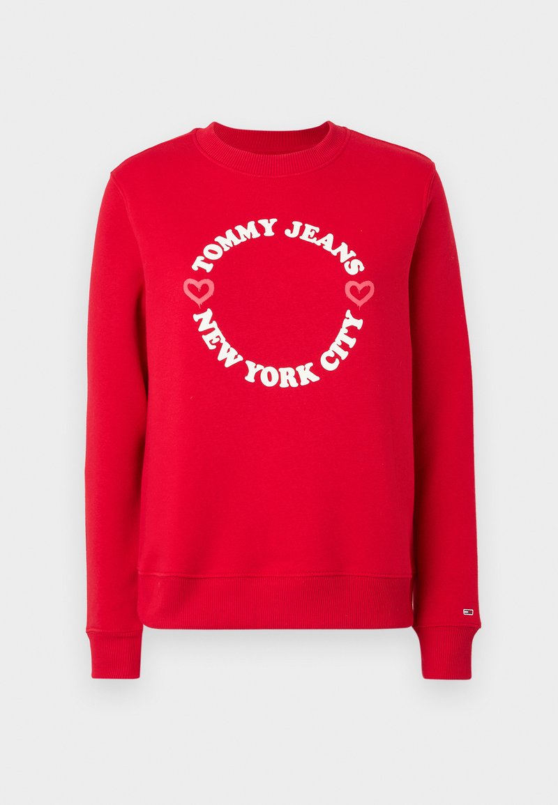 Roter Kapuzenpullover mit geripptem Kragen und Bündchen. Besitzt ein rundes weißes Logo mit dem Schriftzug "TOMMY JEANS" und "NEW YORK CITY", ergänzt durch Herzsymbole.