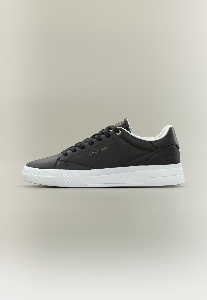 Schwarzer Sneaker mit niedrigem Schaft, weißer Sohle, schwarzen Schnürsenkeln und "GAP EST. 1969" in goldenen Buchstaben an der Seite.