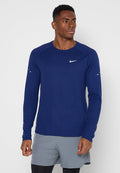 Athletischer Mann trägt ein dunkelblaues Nike Langarmshirt und graue Shorts, steht vor einem schlichten hellen Hintergrund und schaut zur Seite.