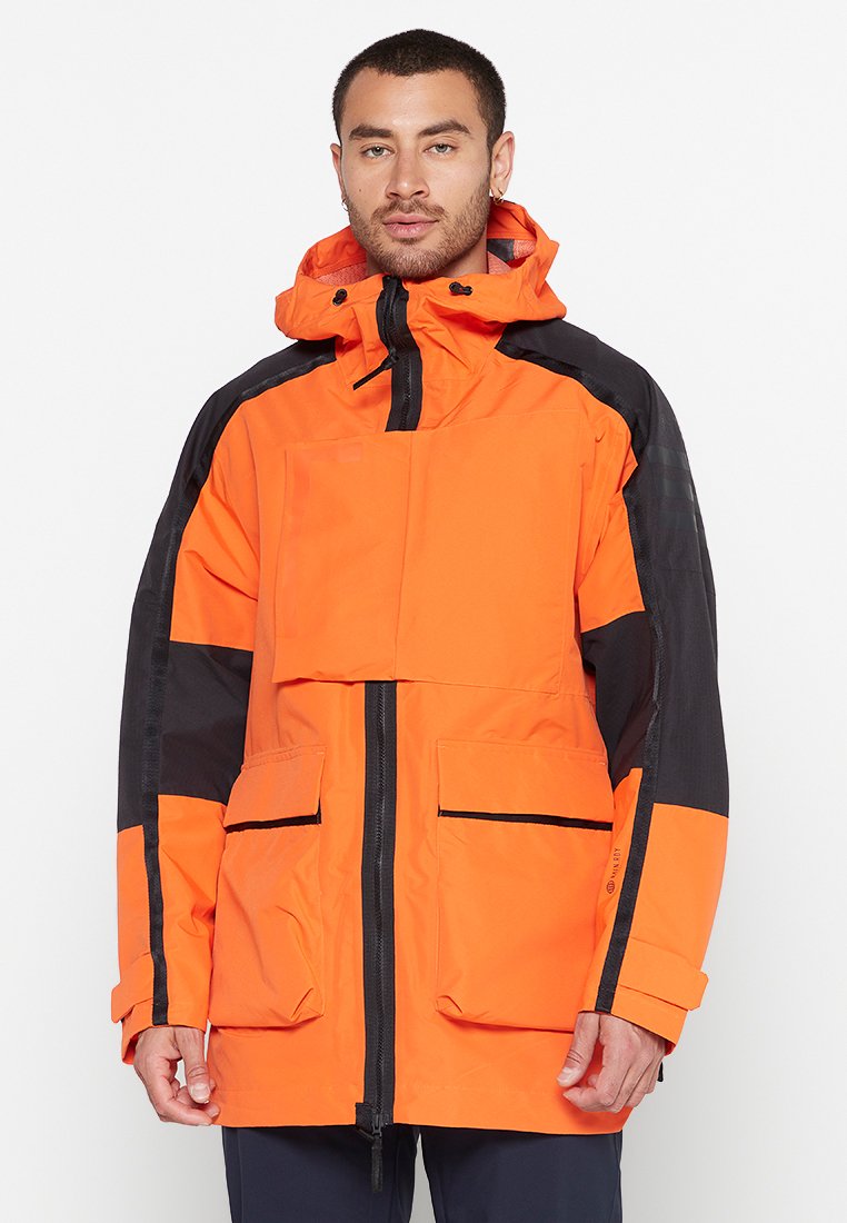 Orangene Jacke mit schwarzen Akzenten, ausgestattet mit einem hohen Kragen, einem Frontreißverschluss und zwei großen Taschen. Aus strapazierfähigem Material mit wasserabweisender Beschichtung.