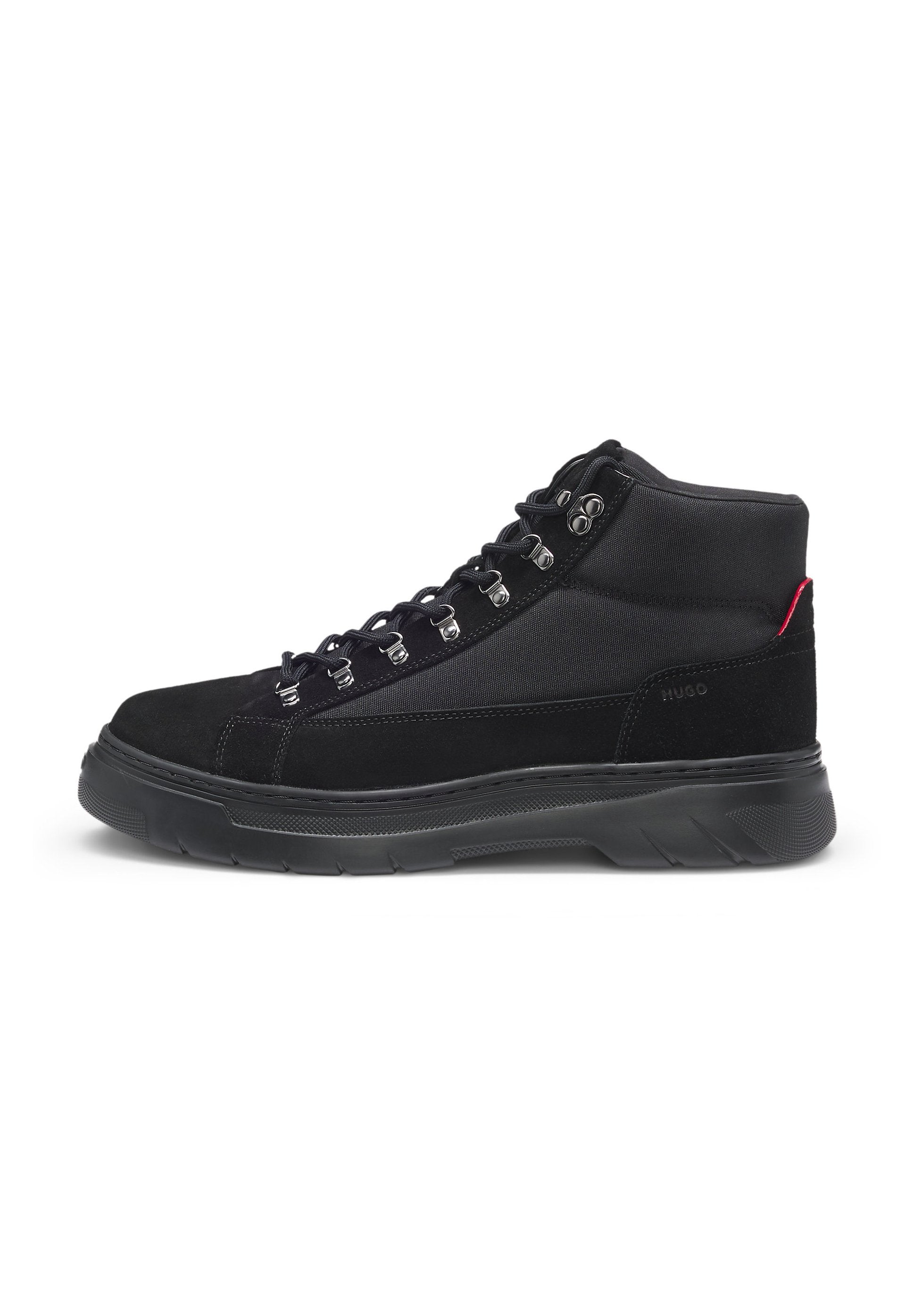 Schwarze High-Top-Sneaker mit Obermaterial aus Wildleder und Stoff, silbernen Metallteilen, Schnürverschluss und einer strukturierten Gummisohle. Pinkfarbener Akzent an der Ferse.