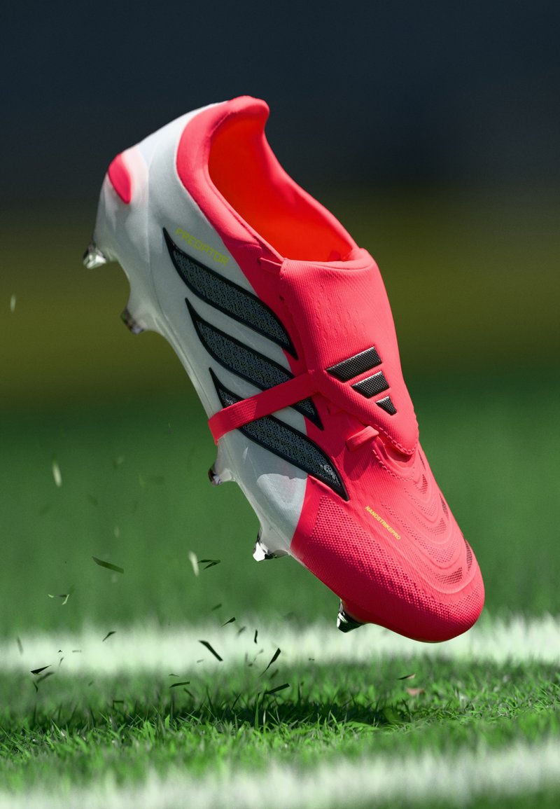 Helles pinkfarbenes Fußballschuh mit einer strukturierten Oberseite, schwarzen Streifen an der Seite und einer weißen Sohle. Stollen sind unter dem Schuh sichtbar.