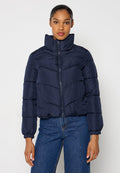 Marineblaue Steppjacke mit hohem Kragen, horizontalem Steppmuster, durchgehendem Reißverschluss und elastischen Bündchen; kombiniert mit blauen Jeans.