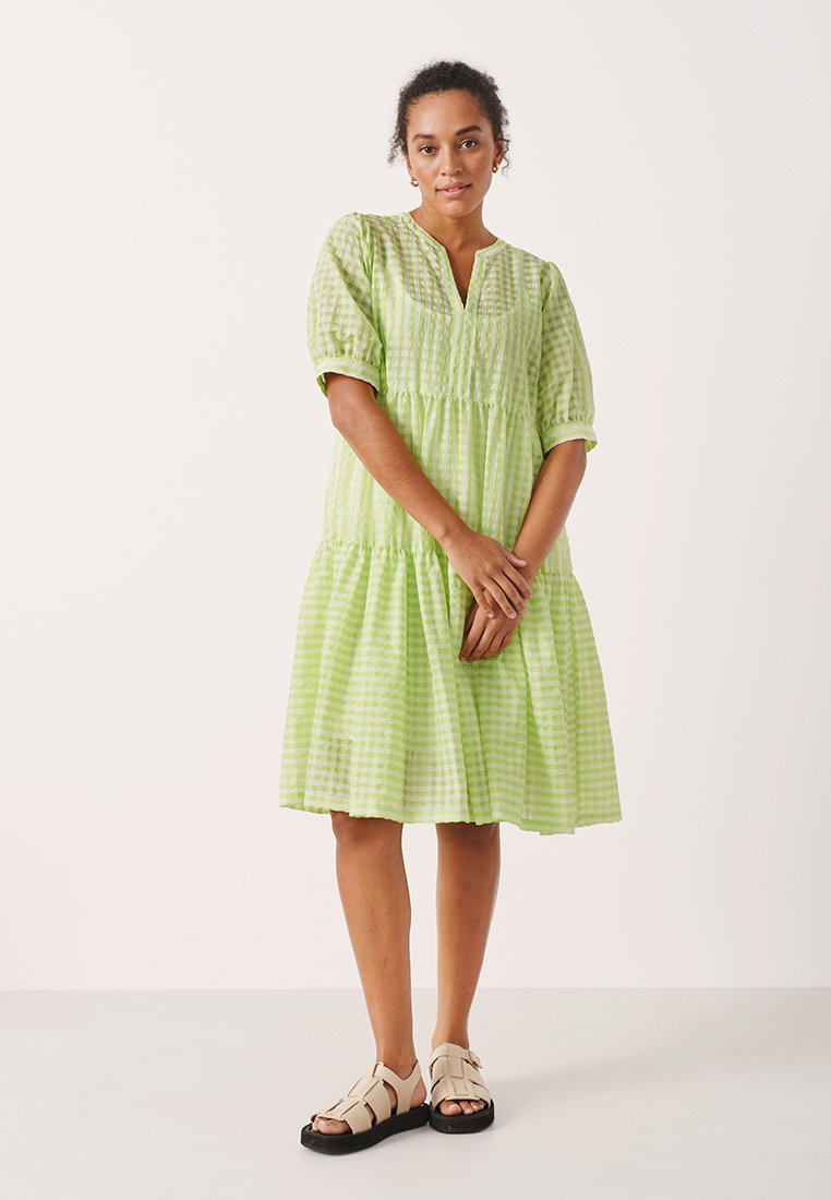 Hellgrünes karierter Kleid mit Puffärmeln, gestuftem Design, leichtem Stoff und V-Ausschnitt. Kombiniert mit beigen Sandalen.