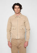 Mann trägt eine beige Wildlederjacke mit Reißverschluss, Kragen und vorderen Klappentaschen, kombiniert mit beigen Hosen, steht vor einem schlichten Hintergrund.
