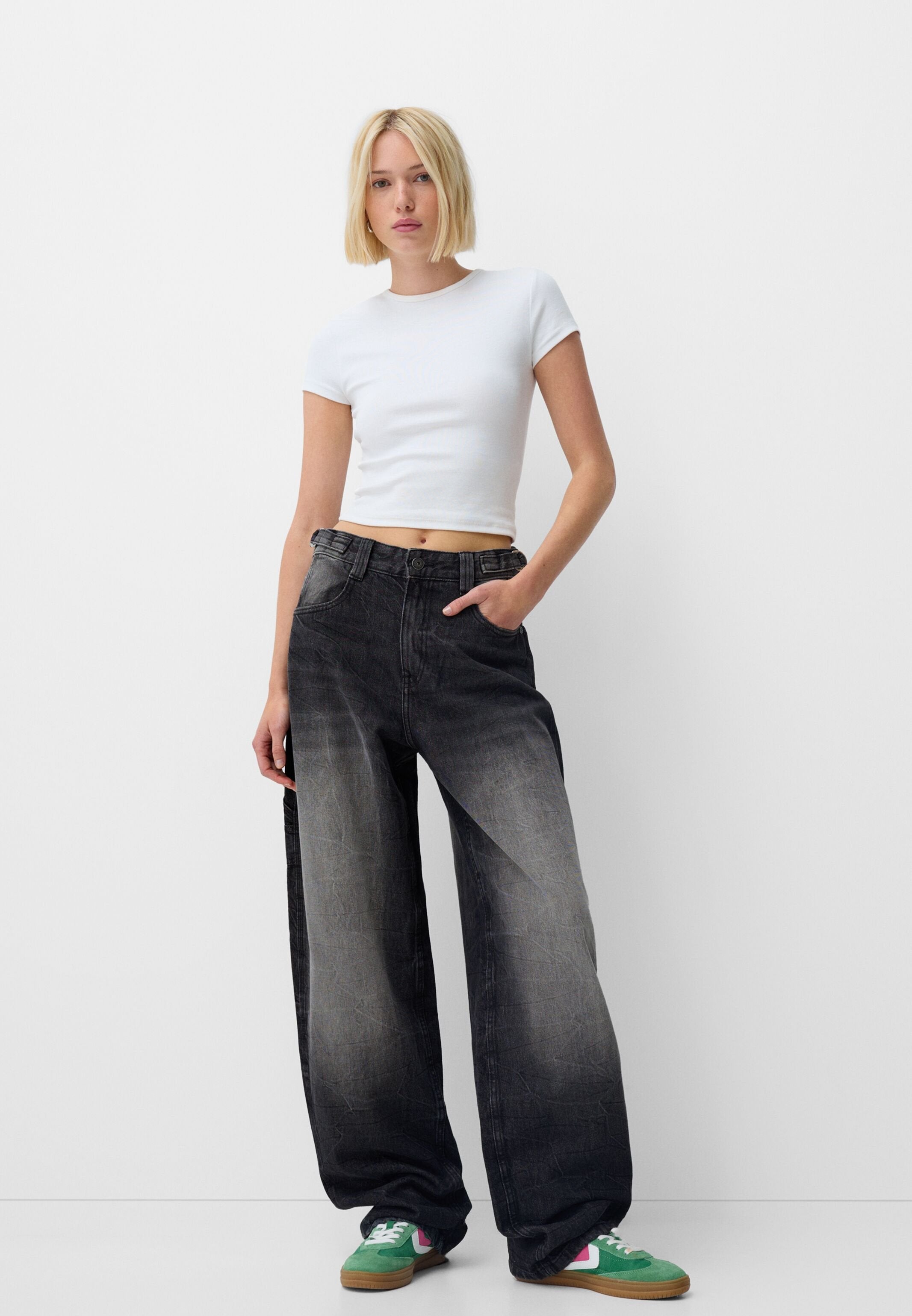 Schwarze weite Jeans mit verwaschenen Details, kombiniert mit einem taillierten weißen Cropped-Top. Enthält einen Knopfverschluss, fünf Taschen und eine lockere Passform.