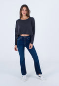 Grauer, verkürzter Pullover mit weiten Ärmeln, kombiniert mit hochgeschnittenen, dunkelblauen Schlagjeans, die seitliche Schlitze haben, und weißen Sneakers.