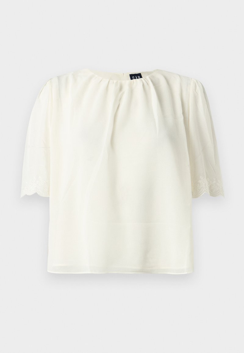 Weiße kurzärmelige Bluse mit gerafftem Ausschnitt und gewellten, bestickten Ärmelsäumen, vor einem schlichten Hintergrund präsentiert.