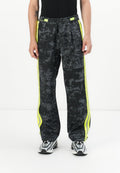 Schwarze Sweatpants mit neon-gelben Seitenstreifen, elastischem Bund und schmal zulaufenden Beinen, kombiniert mit grau-schwarzen Sneakers.